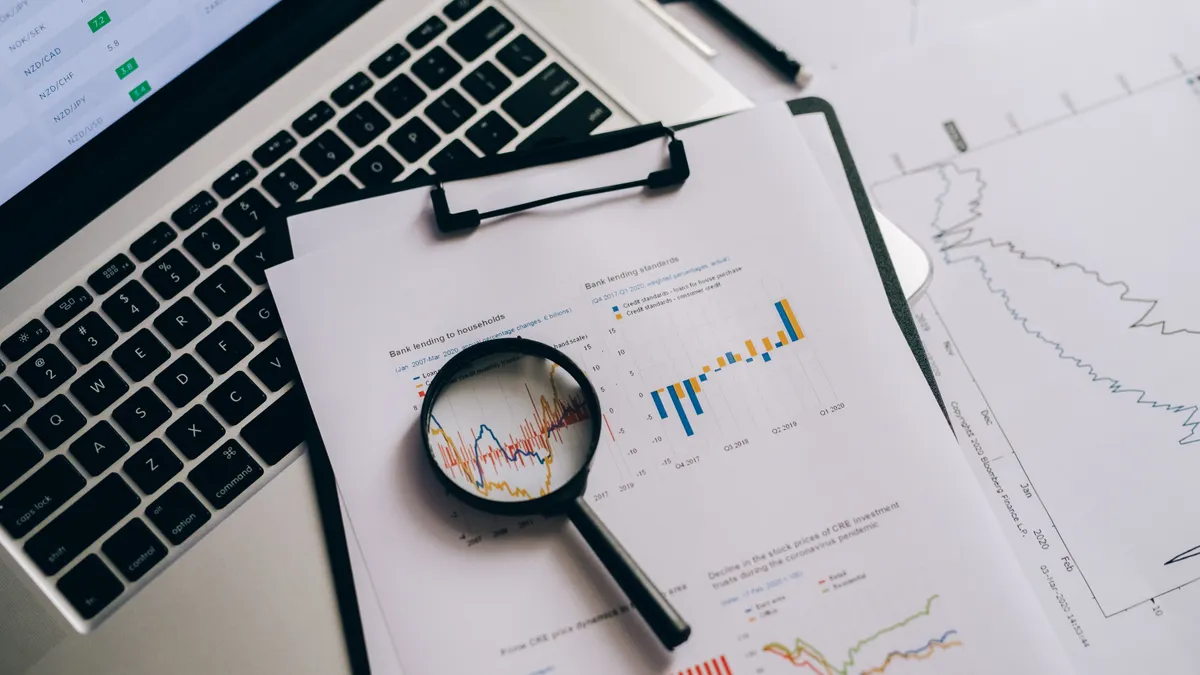 AI article writer plagiarism check: how to review originality before publishing Magnifying glass over printed charts next to a laptop