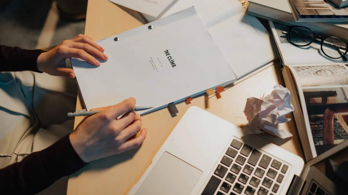 Desk scene with laptop, paper files, and a document being reviewed